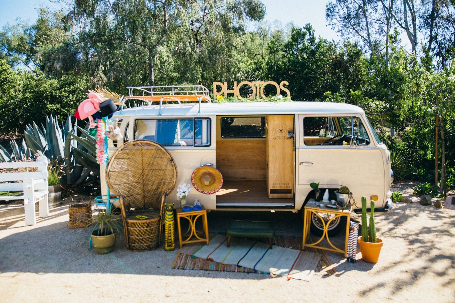 Vintage VW bus photo booth decorated with plants, wicker decor, and a Photos sign at an outdoor event.