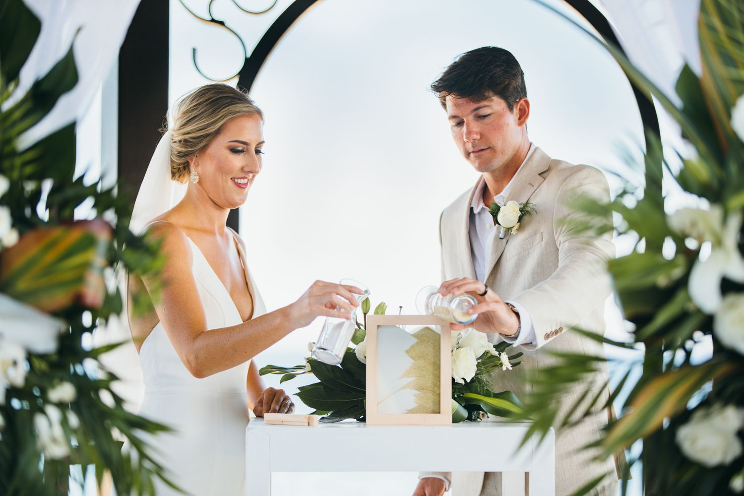 Bride and groom lighting unity candle at outdoor wedding ceremony under floral arch.