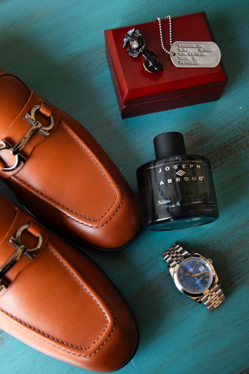 Groom accessories flat lay with tan loafers, Joseph Abboud cologne, Rolex watch, and dog tags.