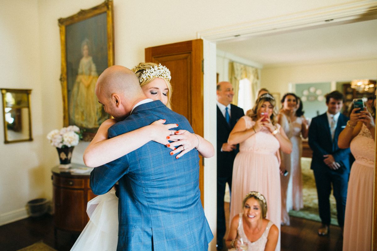 Emotional moment as bride hugs a guest while wedding party looks on in a doorway.