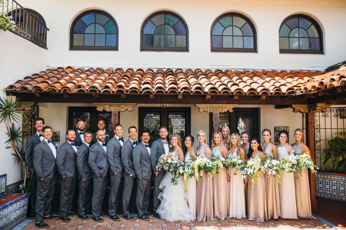 Wedding party posing together outside a Spanish colonial venue with bridesmaids in blush gowns.