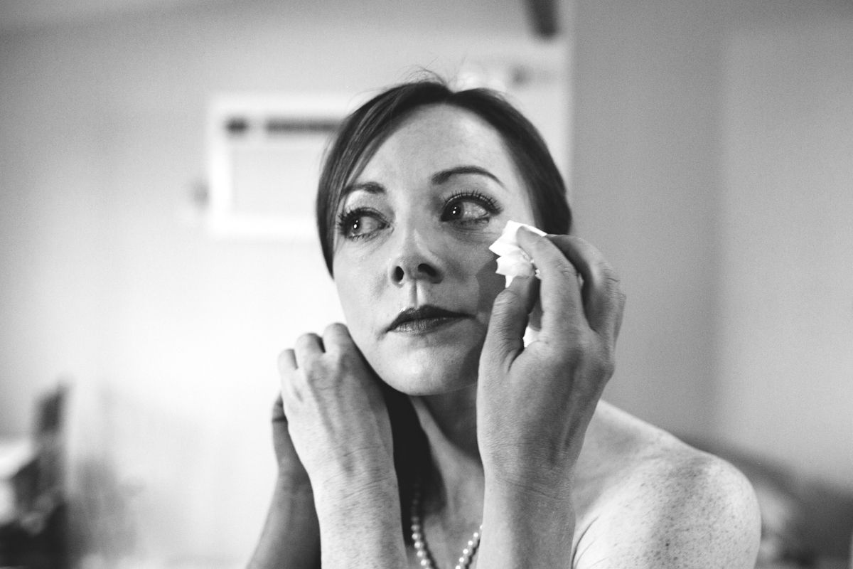 Woman dabbing tears from eyes with tissue in emotional black and white wedding portrait.