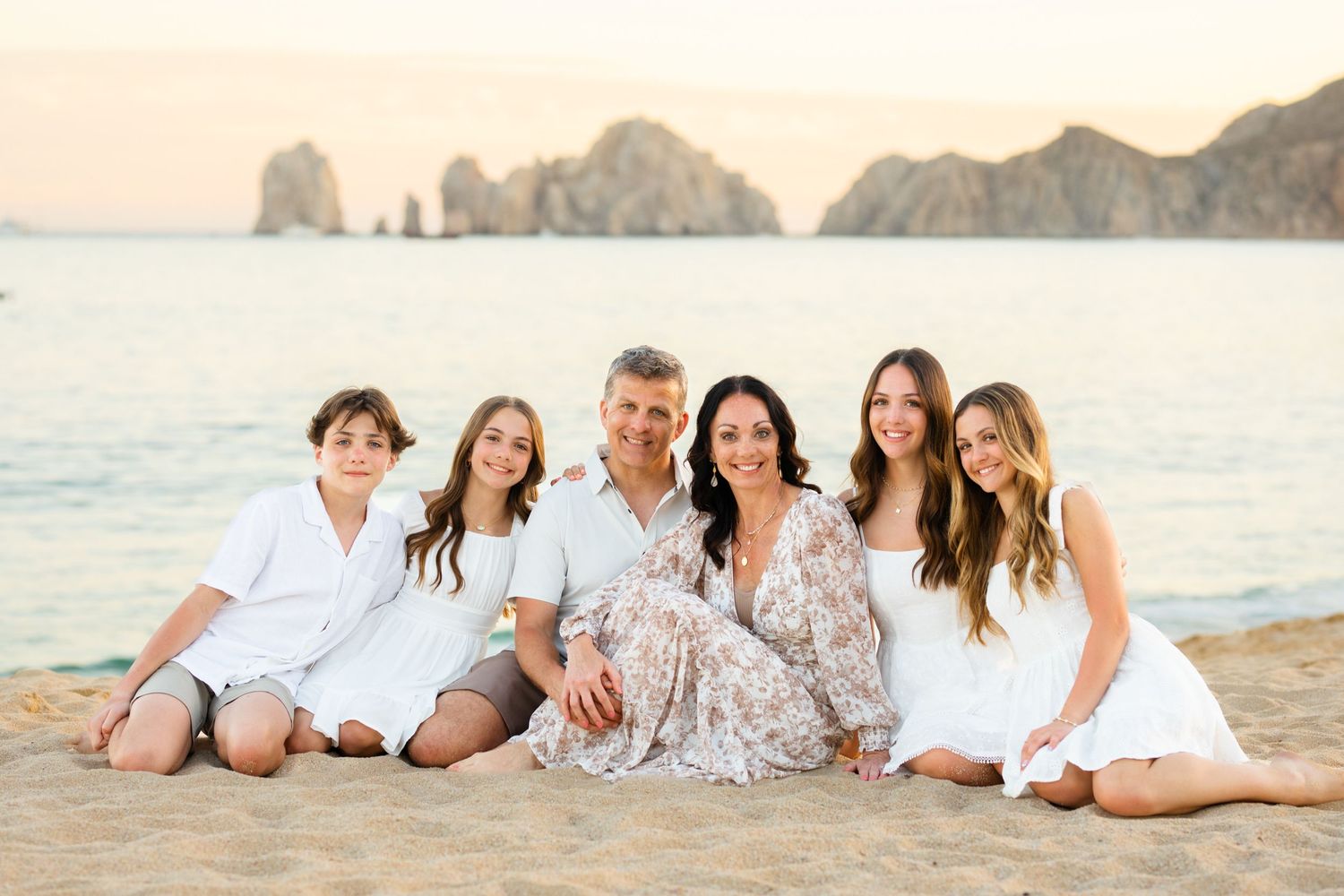 Family of six posing on sandy beach at sunset with rocky cliffs in background at Cabo San Lucas.