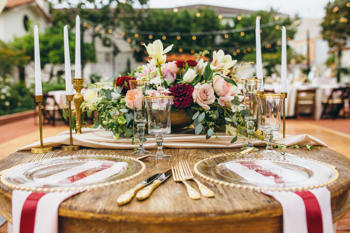Elegant wedding reception tablescape with gold flatware, floral centerpiece, and taper candles.