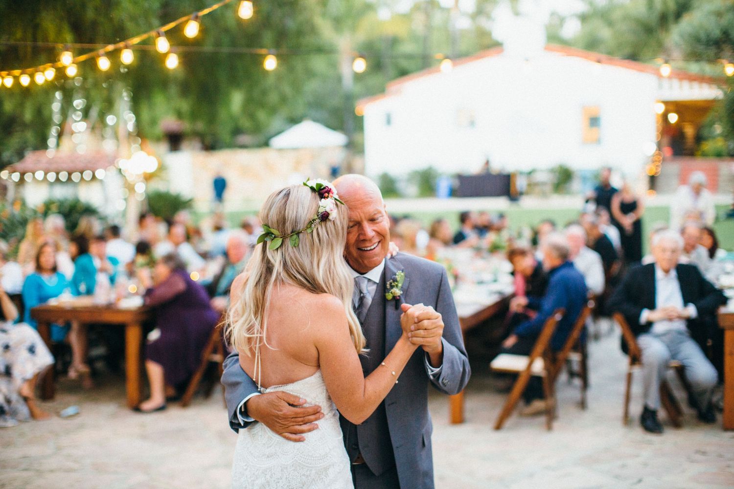 Father-daughter wedding dance at outdoor reception, guests seated at long tables in warm evening setting at Leo Carrillo ranch