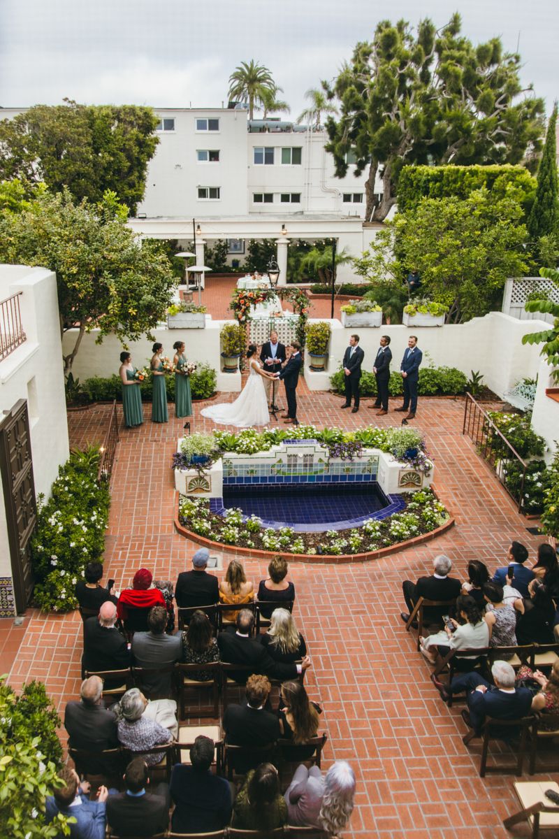 Aerial view of outdoor wedding ceremony with guests seated around a fountain at a Spanish-style venue.