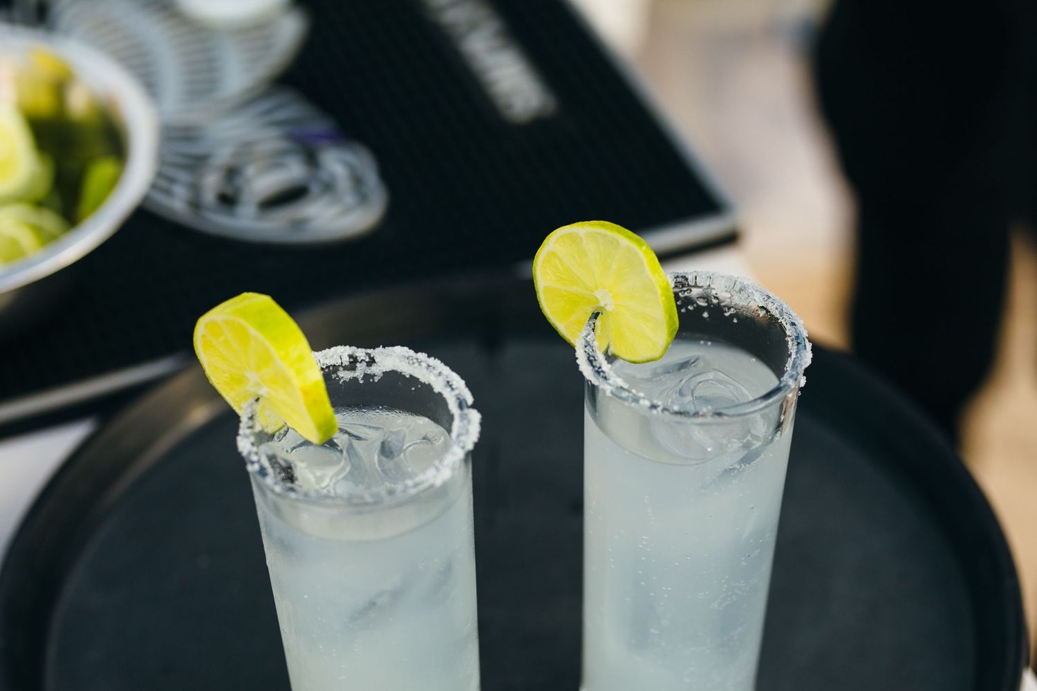 Two salted rim cocktail glasses garnished with lime slices served on a dark tray.
