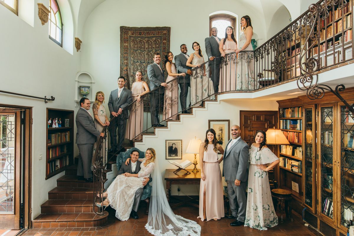 Wedding party posed on grand staircase in elegant library venue with bridesmaids and groomsmen.