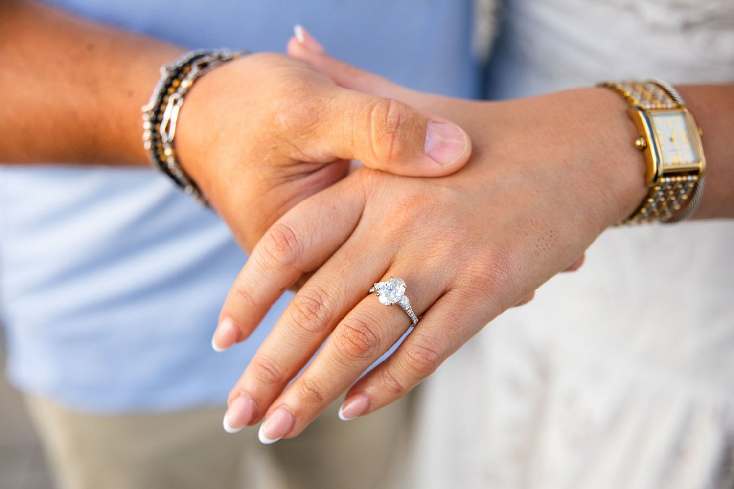Close-up of a woman's hand displaying a diamond engagement ring, with a man's hand resting behind hers.