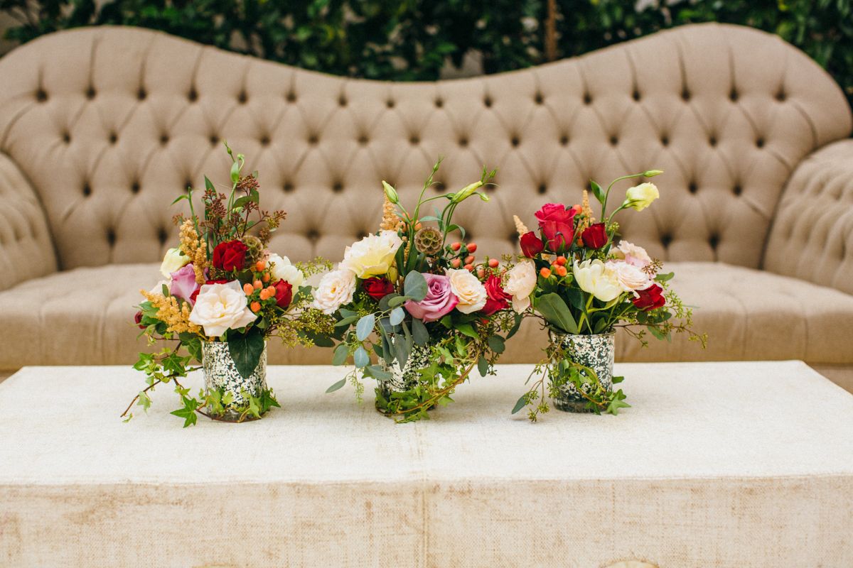 Three colorful floral arrangements with roses and greenery displayed on white table at wedding.