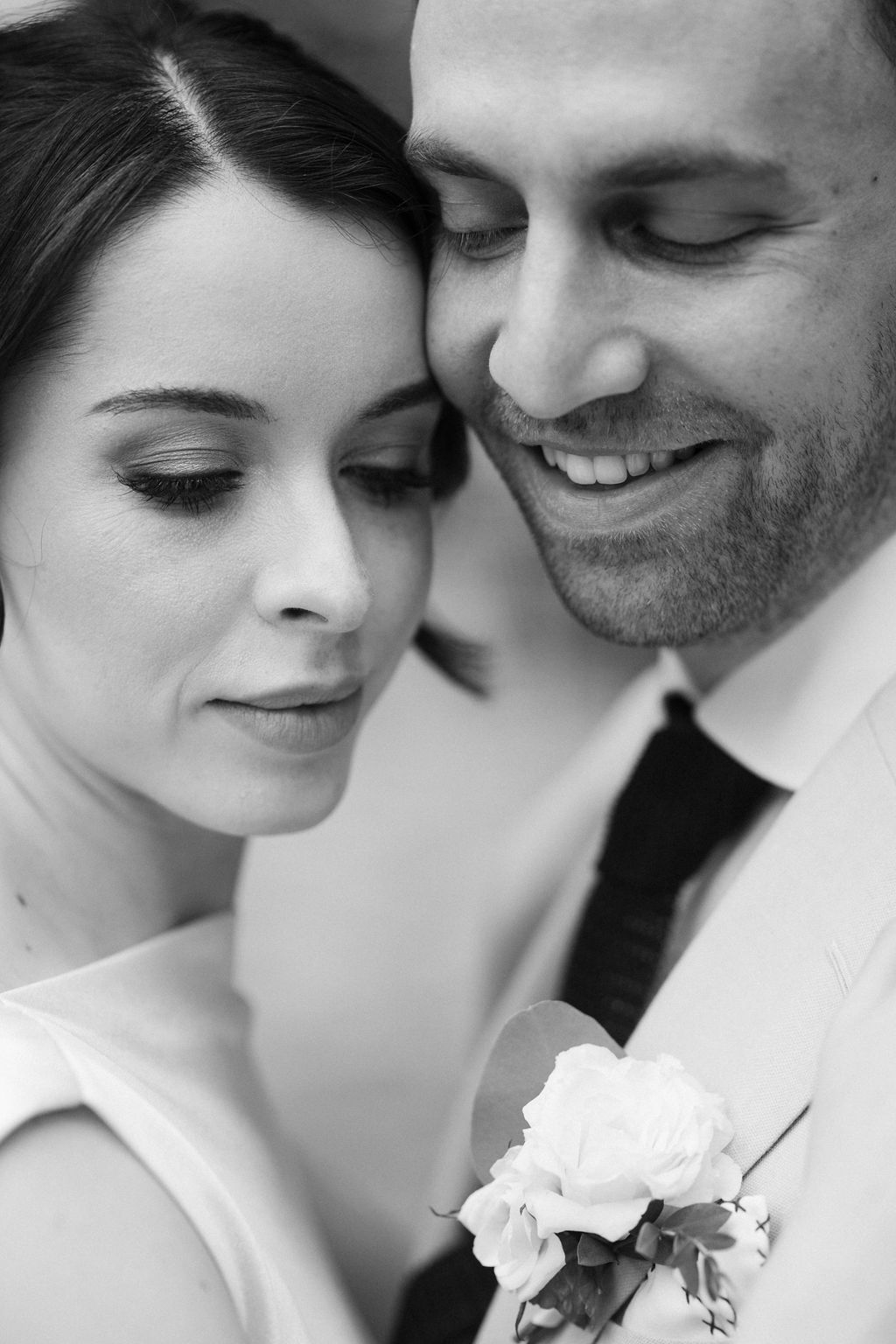 Intimate black and white portrait of smiling groom and bride with elegant makeup and boutonniere.