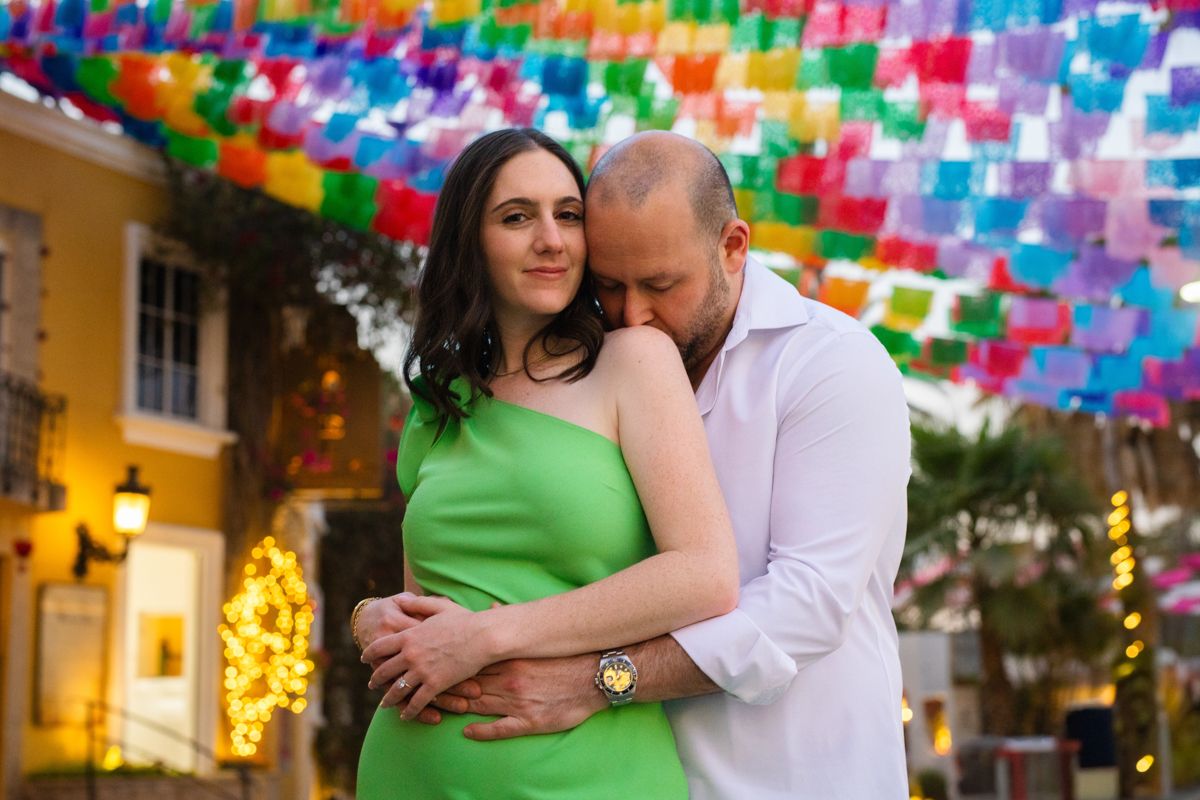 Couple embracing under colorful papel picado banners on a festive Mexican street at night.