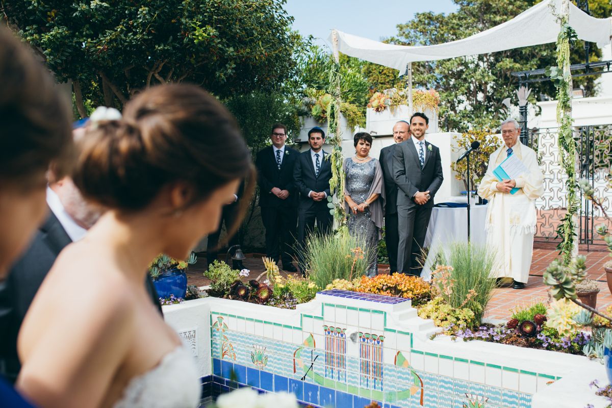 Outdoor wedding ceremony in a garden with guests seated and officiant at a floral decorated altar.