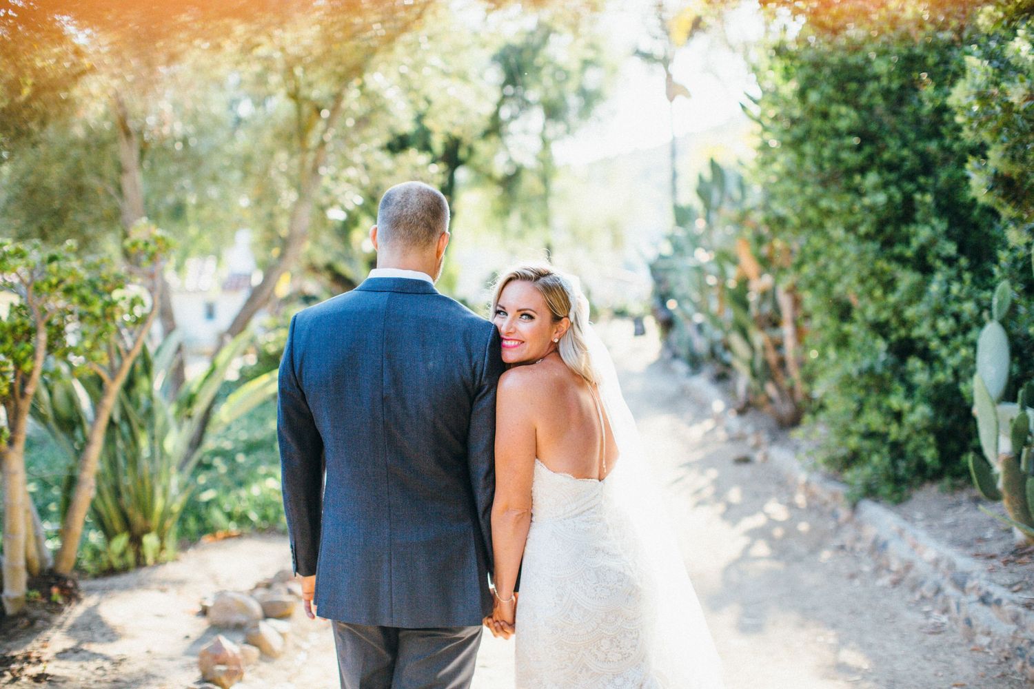 Bride and groom walking hand in hand along a scenic garden path, bride glancing back over her shoulder at Leo Carrillo ranch wedding