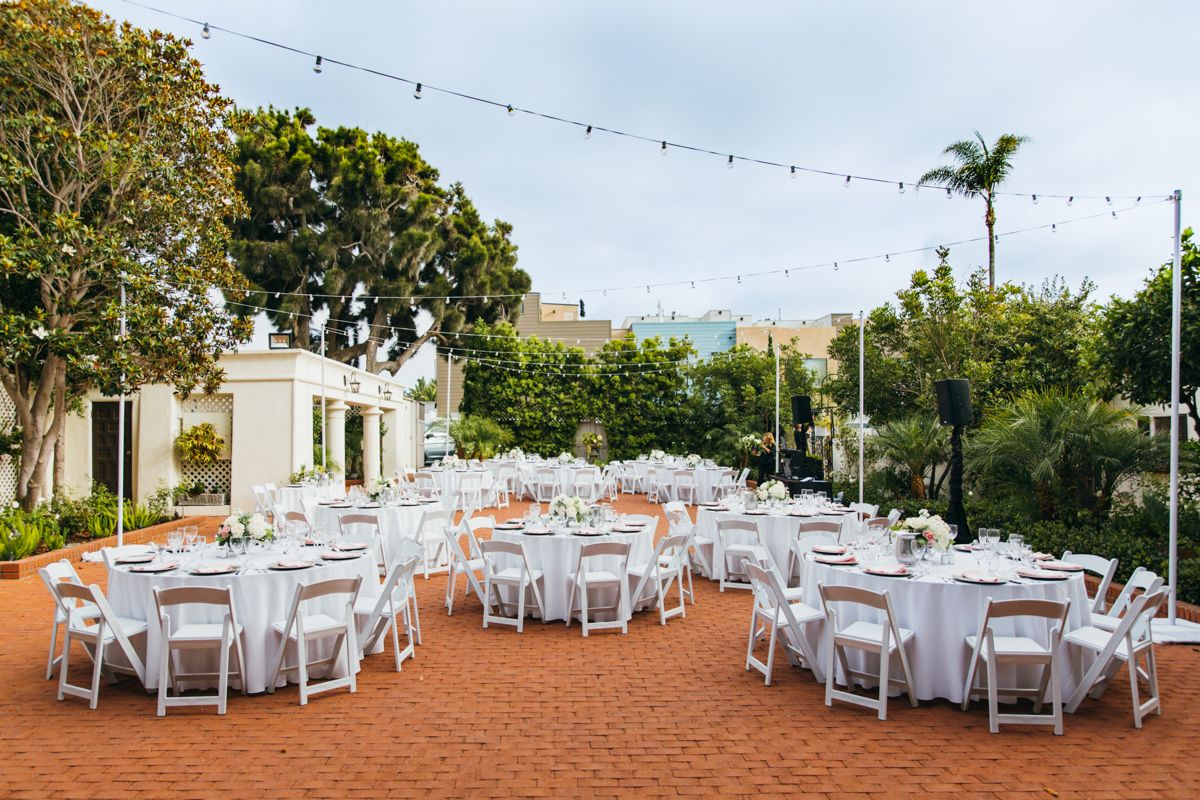 Outdoor wedding reception with white round tables and chairs on brick patio with string lights.