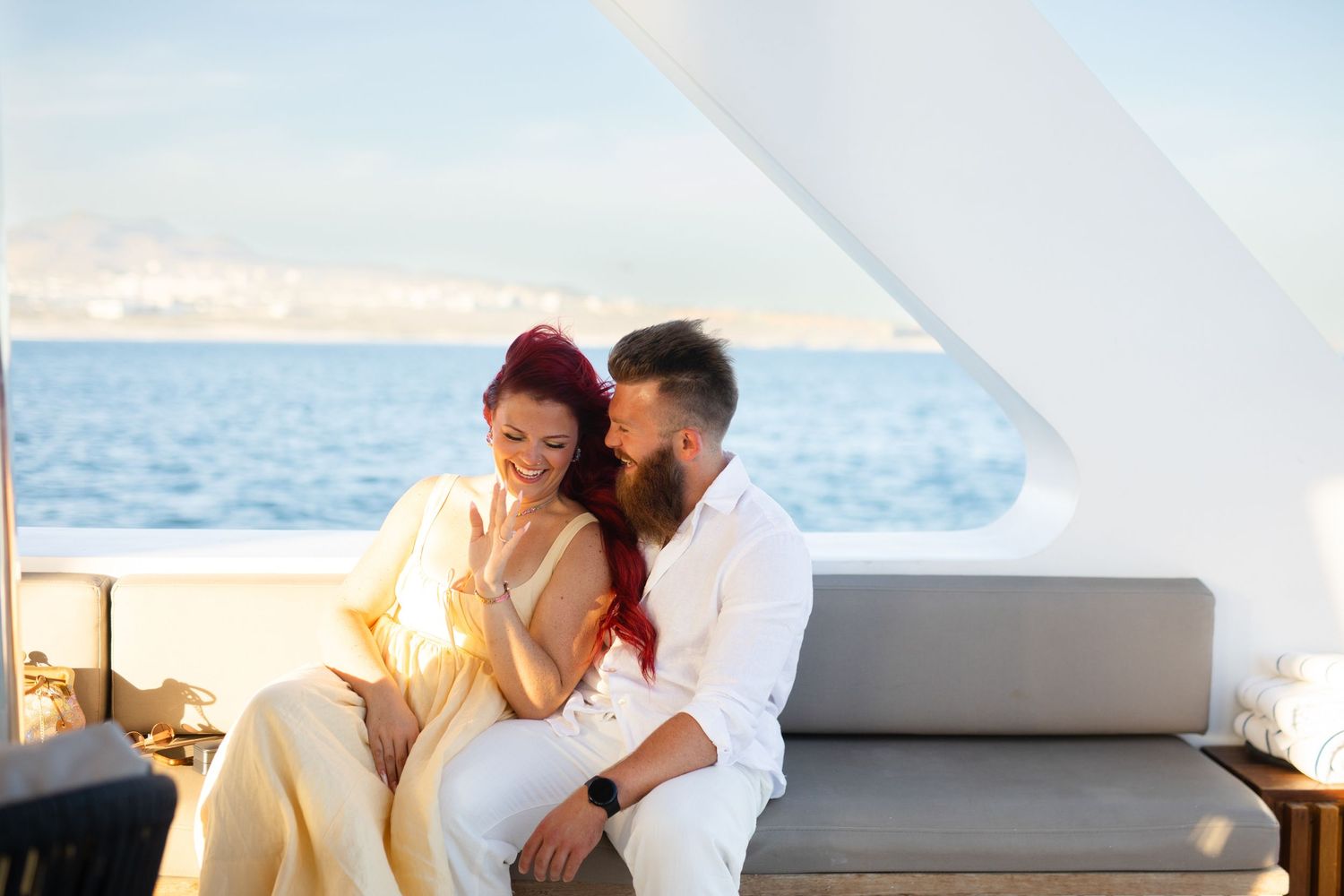 Couple sitting together on a yacht deck, smiling and laughing with ocean views in the background.