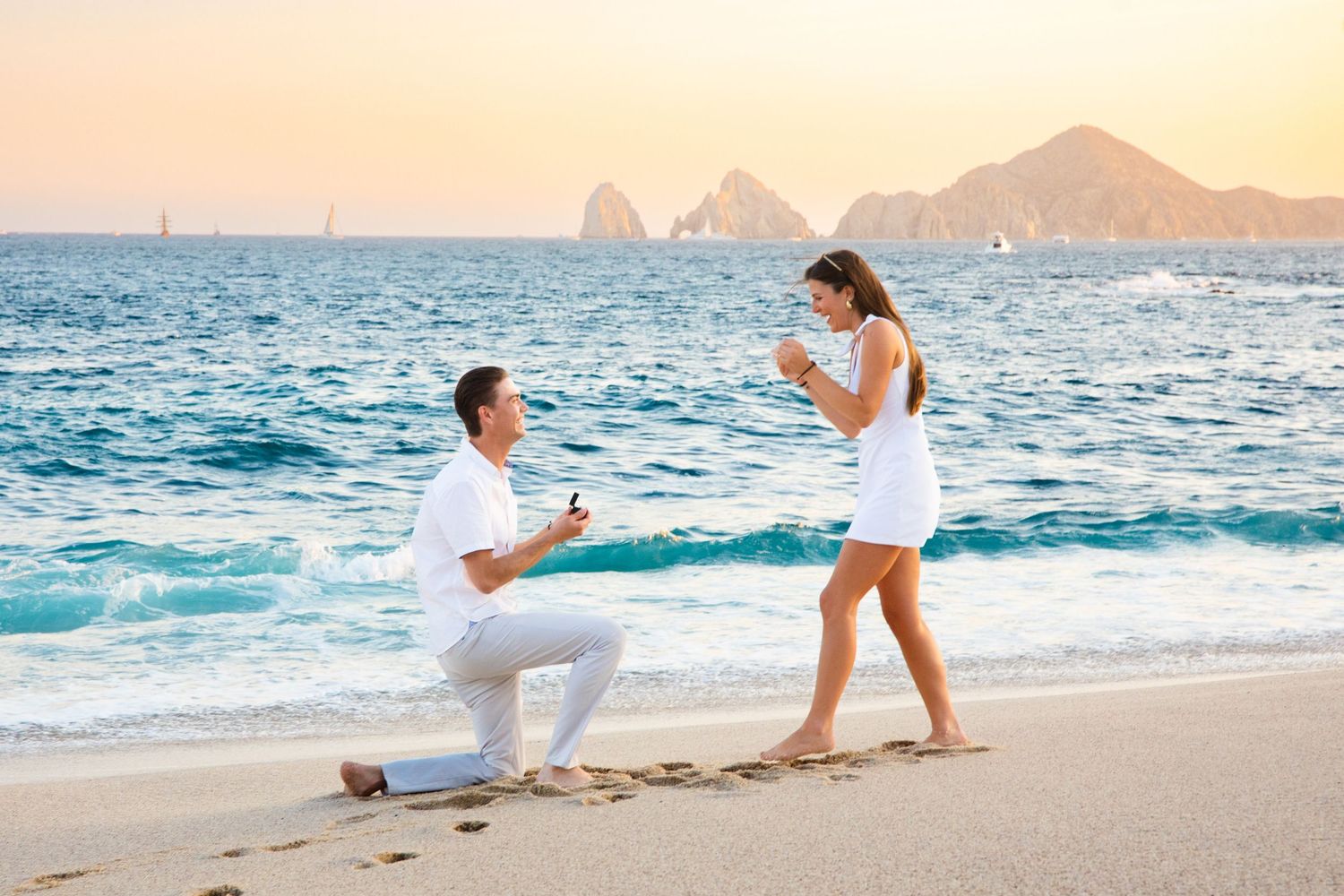 Man proposing on one knee to woman on a beach at sunset in Cabo San Lucas.