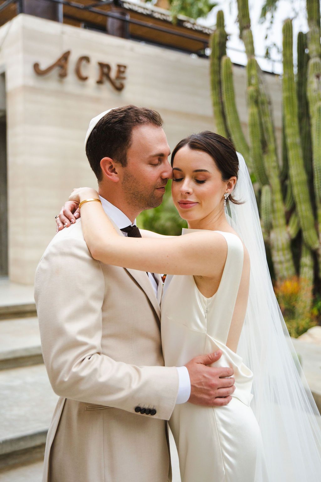 Bride and groom embracing tenderly outside the Acre venue surrounded by lush tropical greenery.