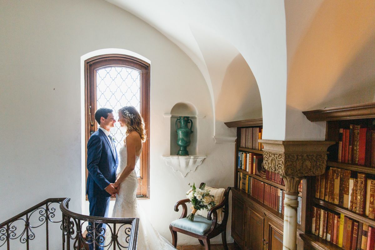 Bride and groom share an intimate moment by a latticed window in a charming library staircase alcove.
