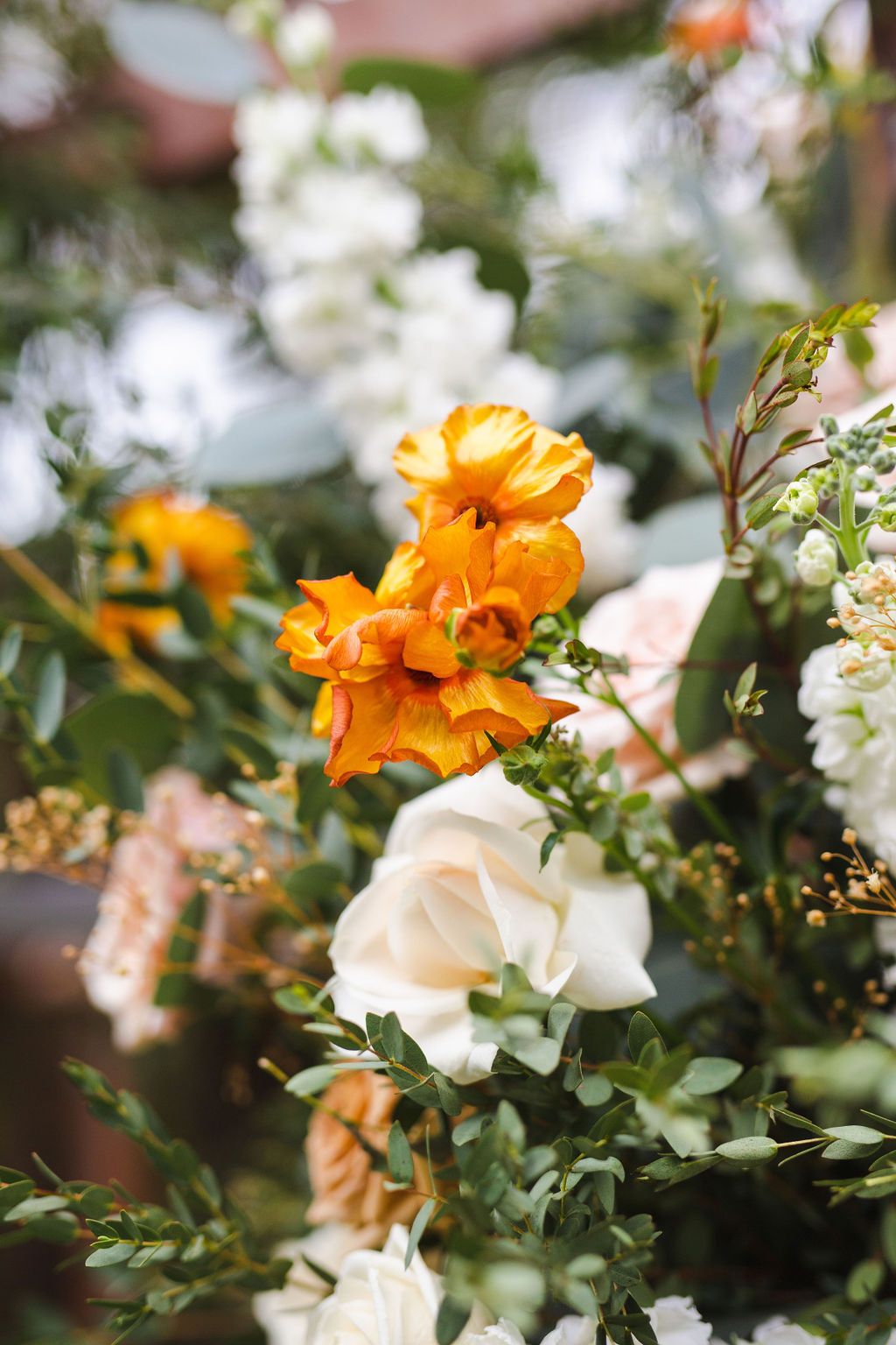 Close-up of vibrant orange and white roses with eucalyptus greenery in a wedding floral arrangement.