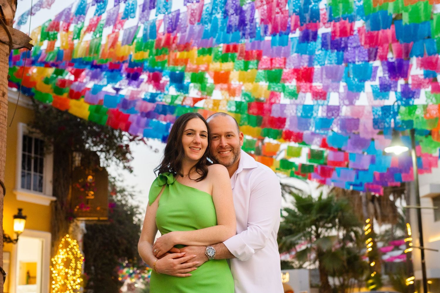 Couple embracing under colorful papel picado flags at a festive evening outdoor setting.