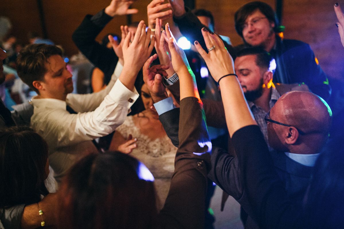 Wedding guests raising hands together in joyful celebration on colorful dance floor.