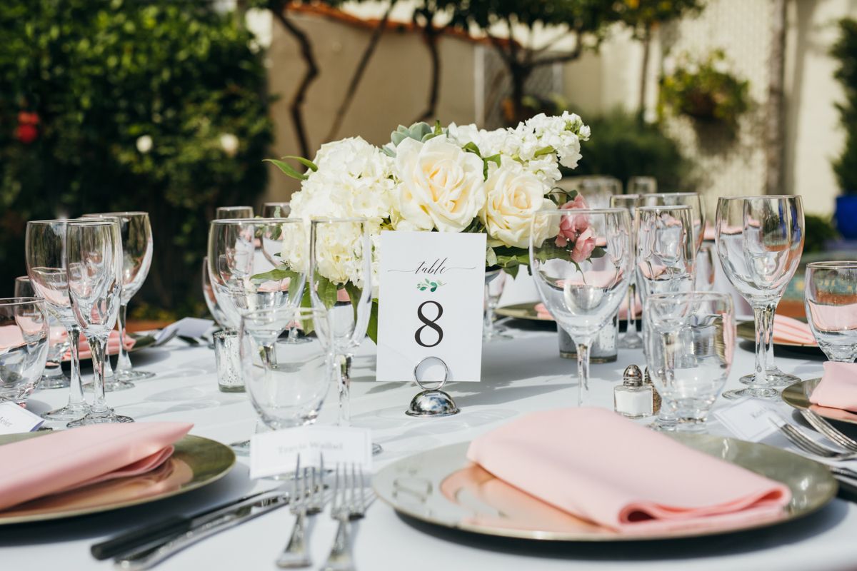 Elegant round wedding reception table with white rose centerpiece, pink napkins, and crystal glassware setting.