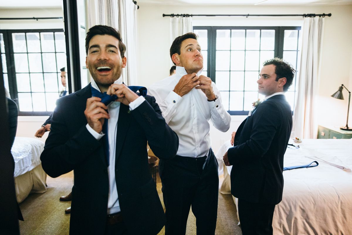 Groomsmen adjusting bow ties together while getting ready for wedding ceremony.