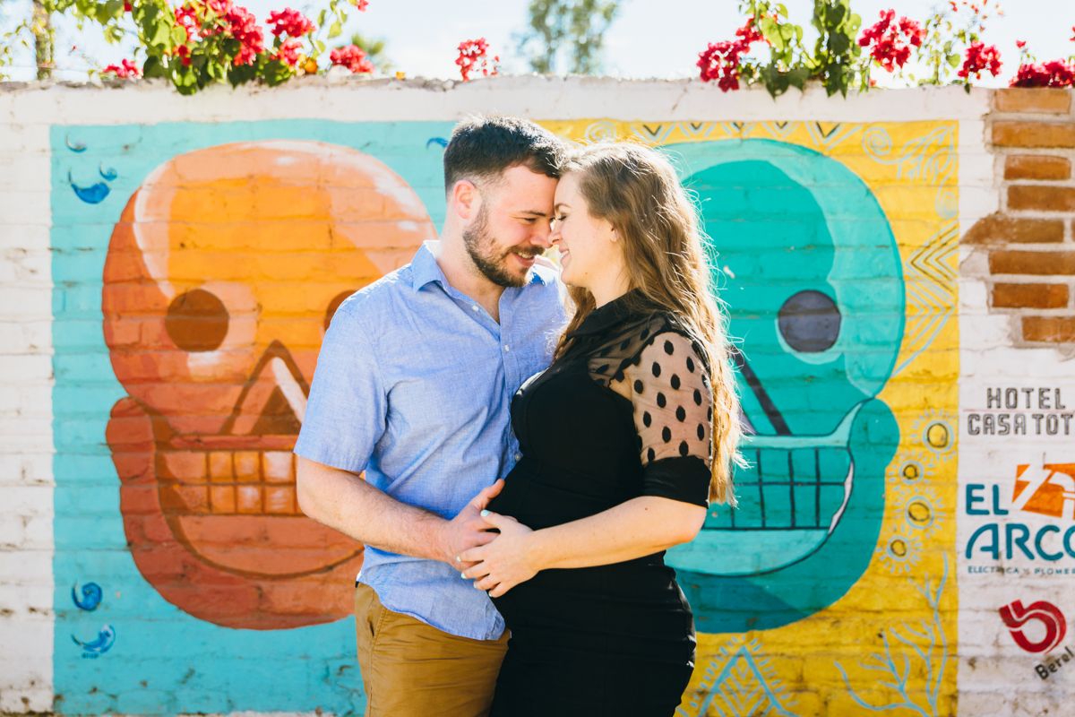 Couple sharing a tender moment in front of vibrant Day of the Dead skull mural.