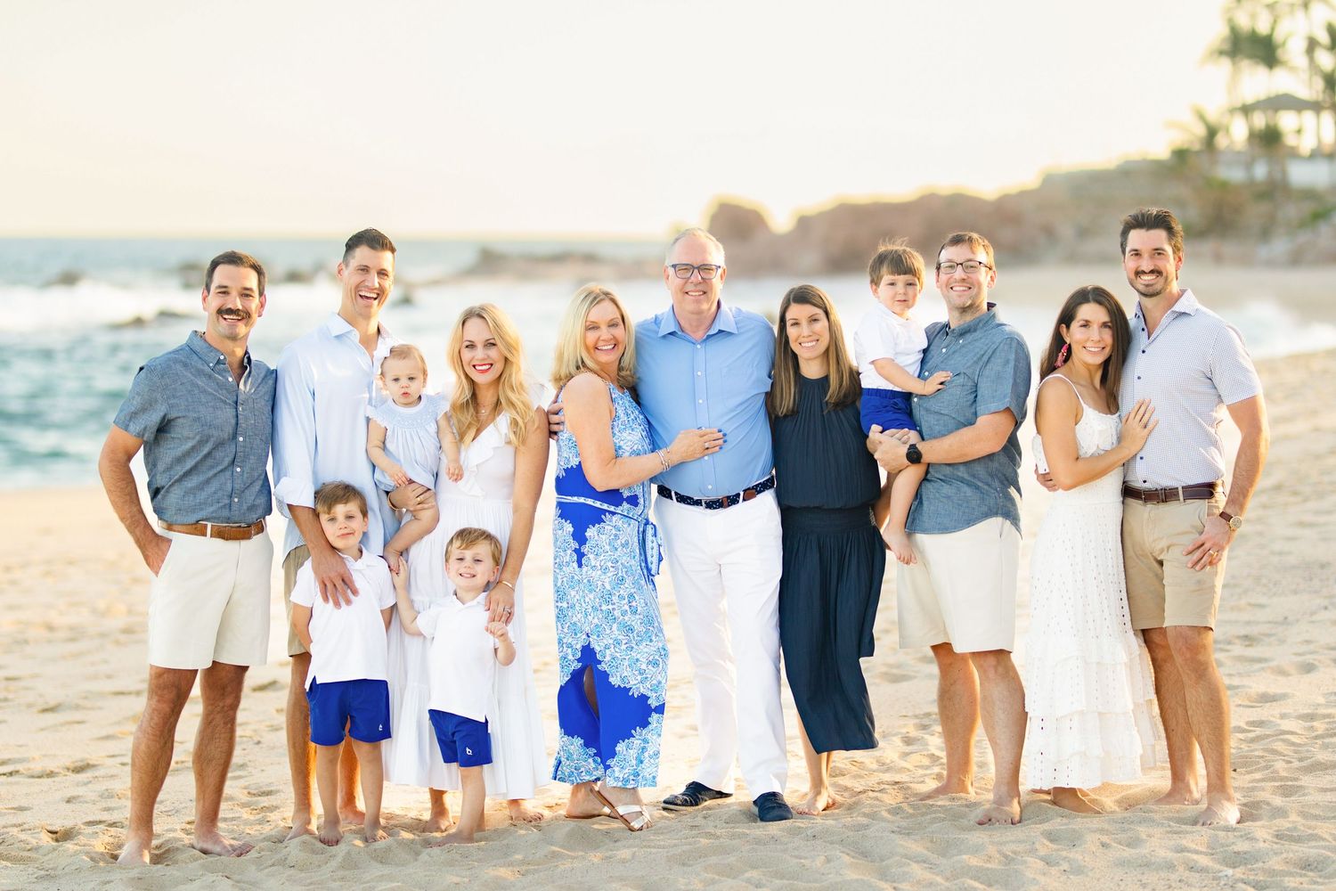 Large family group portrait on a sandy beach in cabo at sunset, wearing coordinated blue and white outfits.