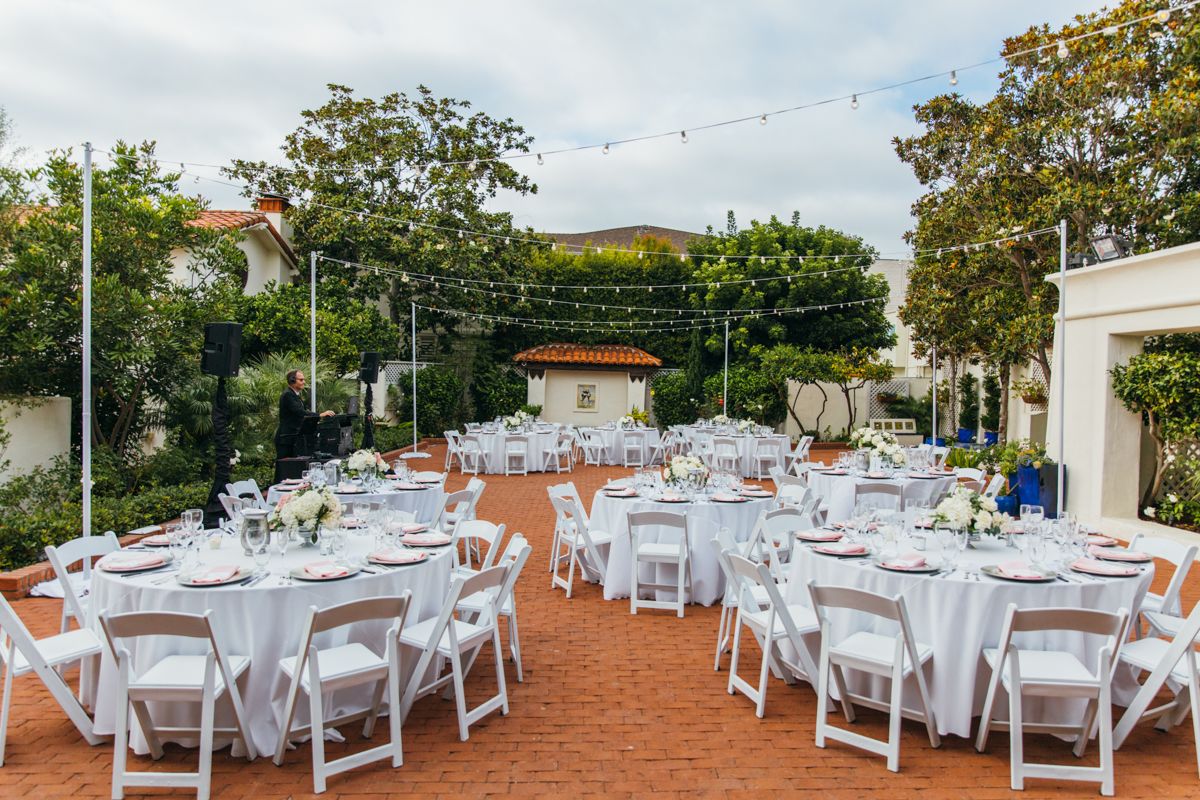 Elegant outdoor wedding reception setup with white tables, chairs, and string lights at dusk.