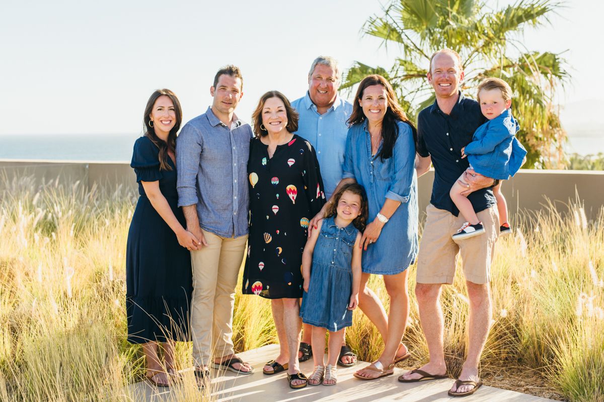 Multi-generational family portrait at golden hour on coastal boardwalk with ocean backdrop.