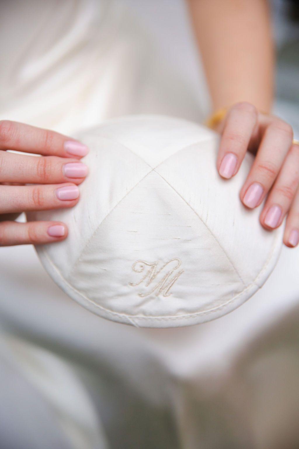 Close-up of a white monogrammed Jewish kippah being held by a bride with manicured pink nails.