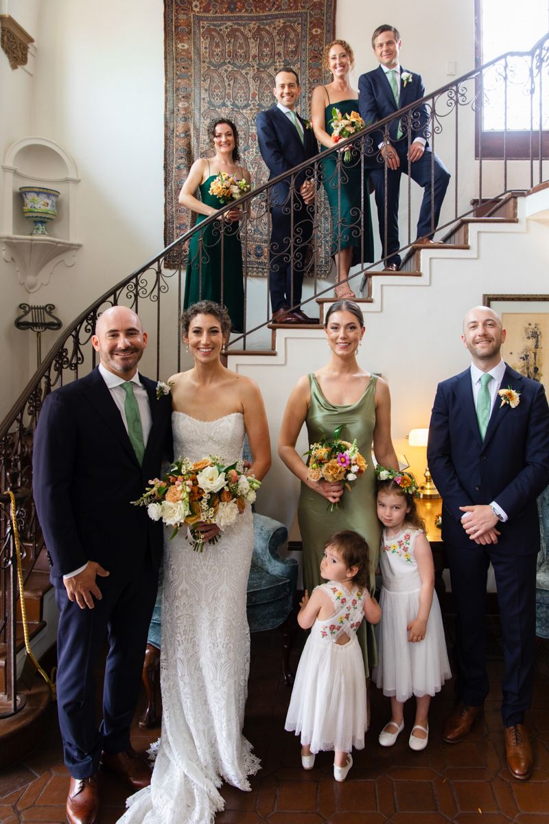 Wedding party poses on spiral staircase with green bridesmaid dresses and flower girls.