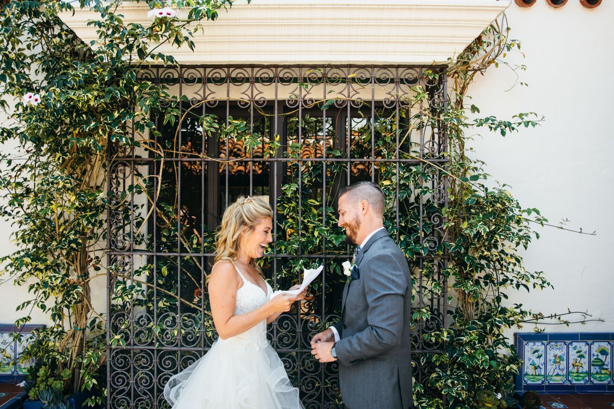Bride and groom exchanging personal vows in front of an ornate iron gate covered in greenery.