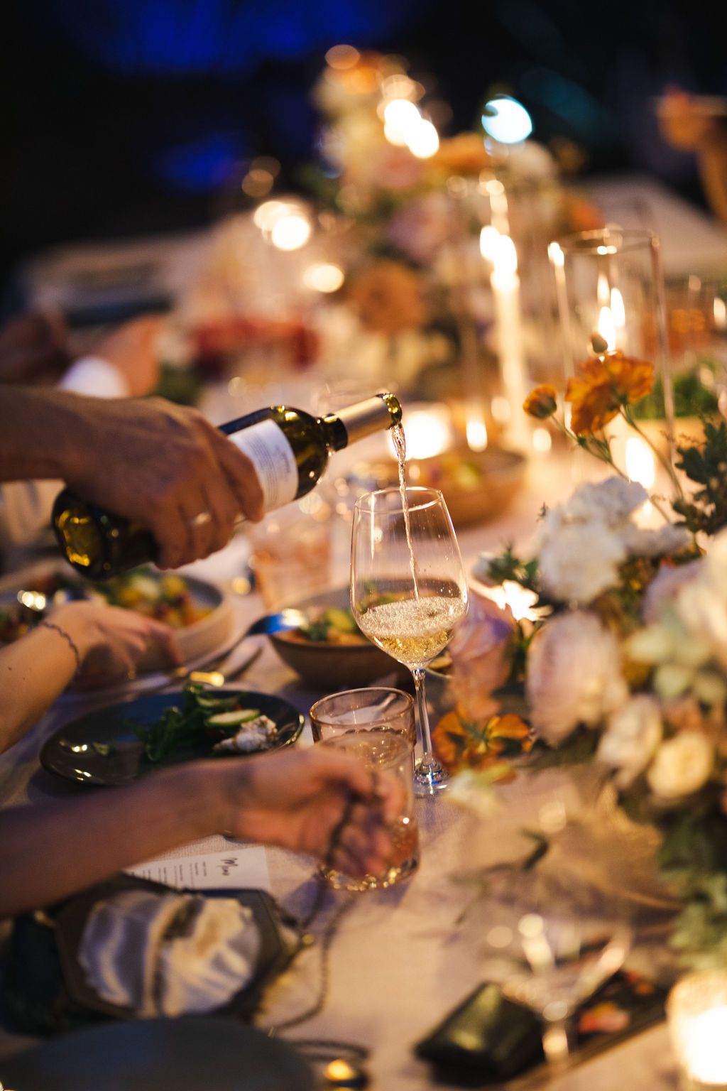 Elegant wedding reception dinner table with candles and florals as wine is poured into a crystal glass.