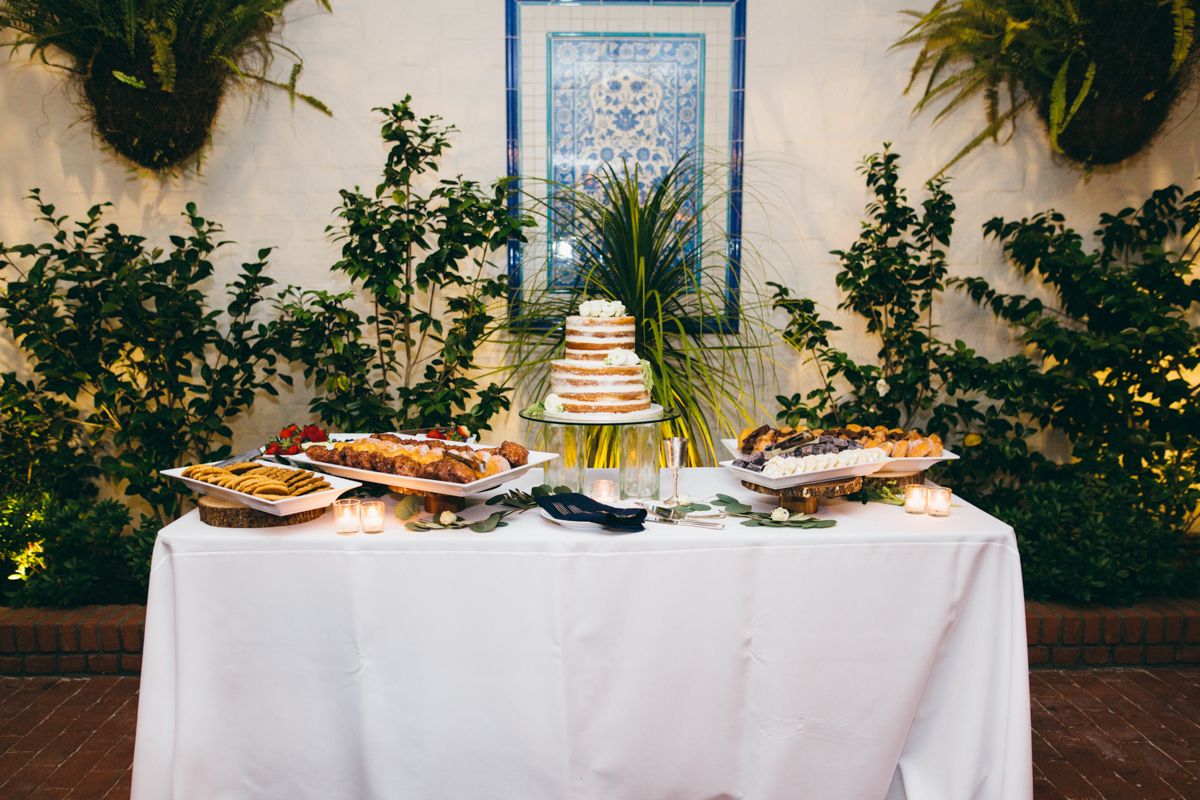 Wedding dessert table with naked cake and assorted treats against a vine-covered white garden wall.