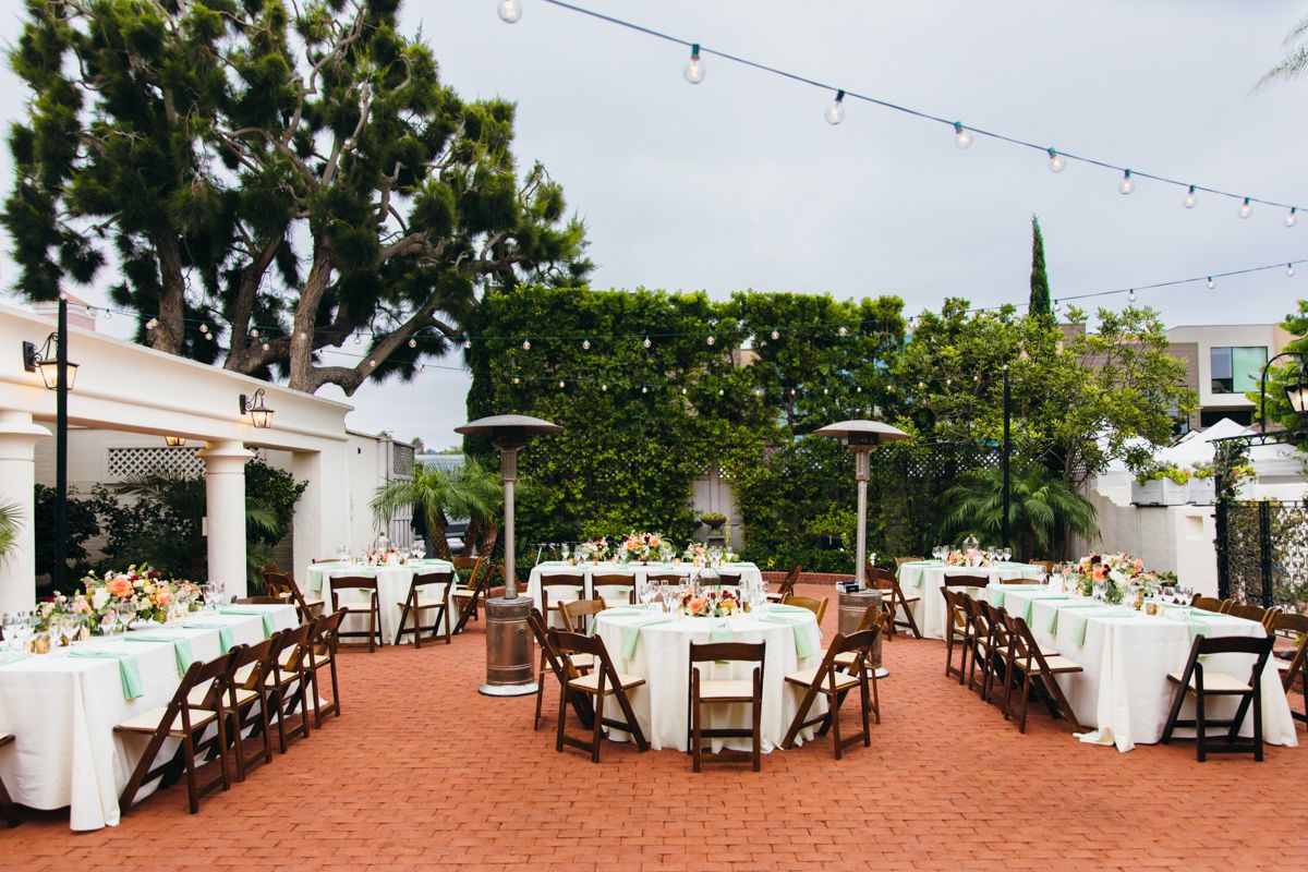 Outdoor wedding reception setup with mix of long and round tables, wooden chairs, patio heaters, and string lights.