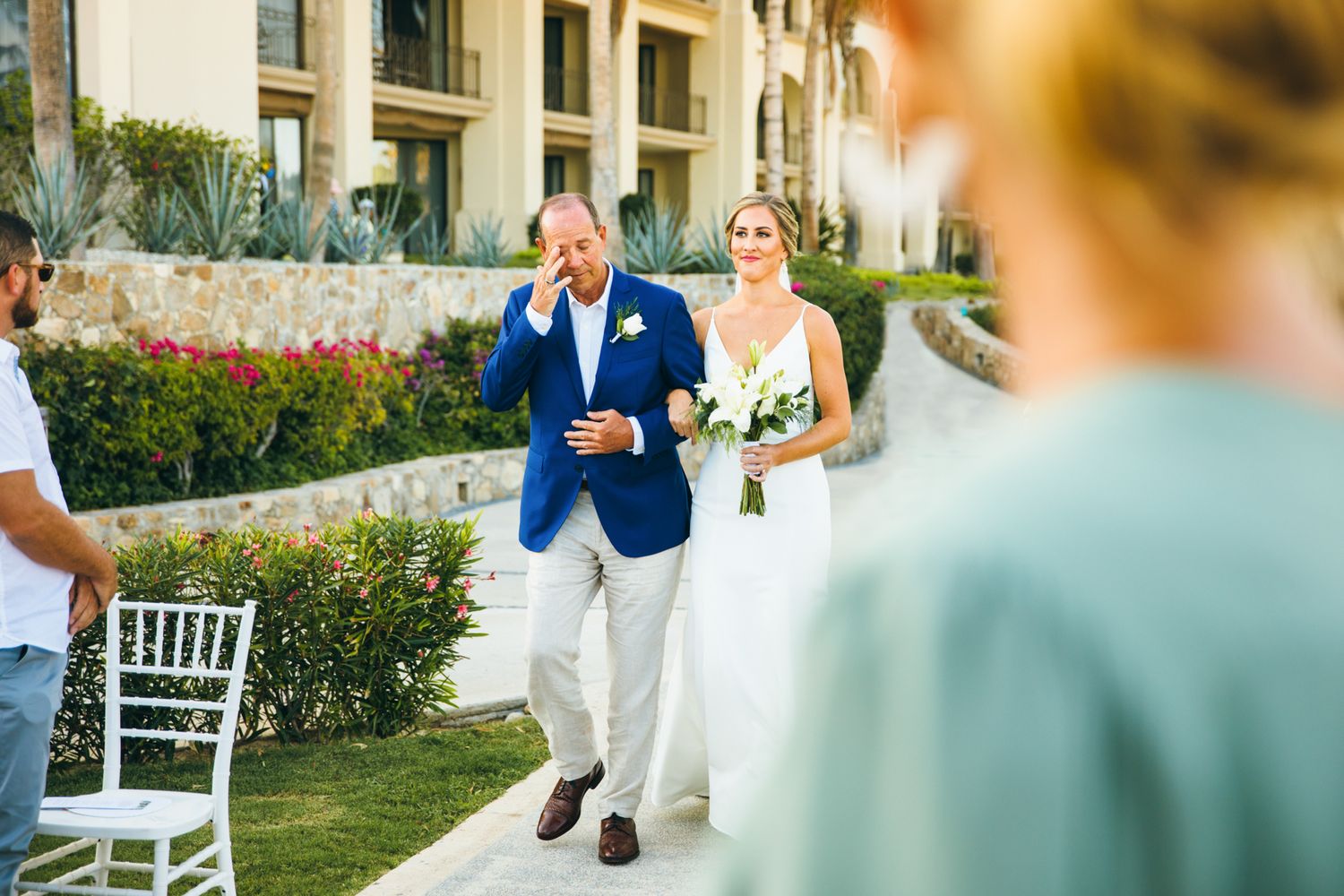 Emotional father walks bride down the aisle at outdoor wedding ceremony at luxury resort.