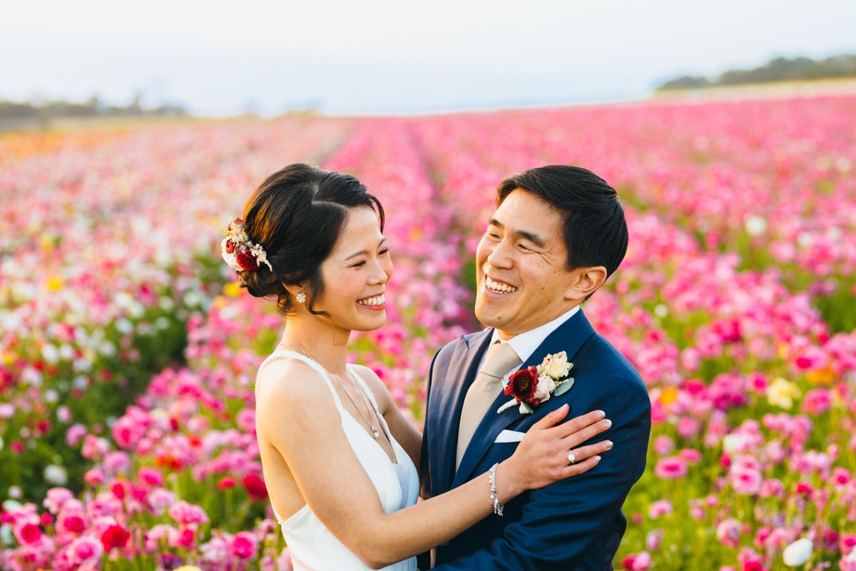 Joyful couple embraces and smiles in a vibrant pink ranunculus flower field.