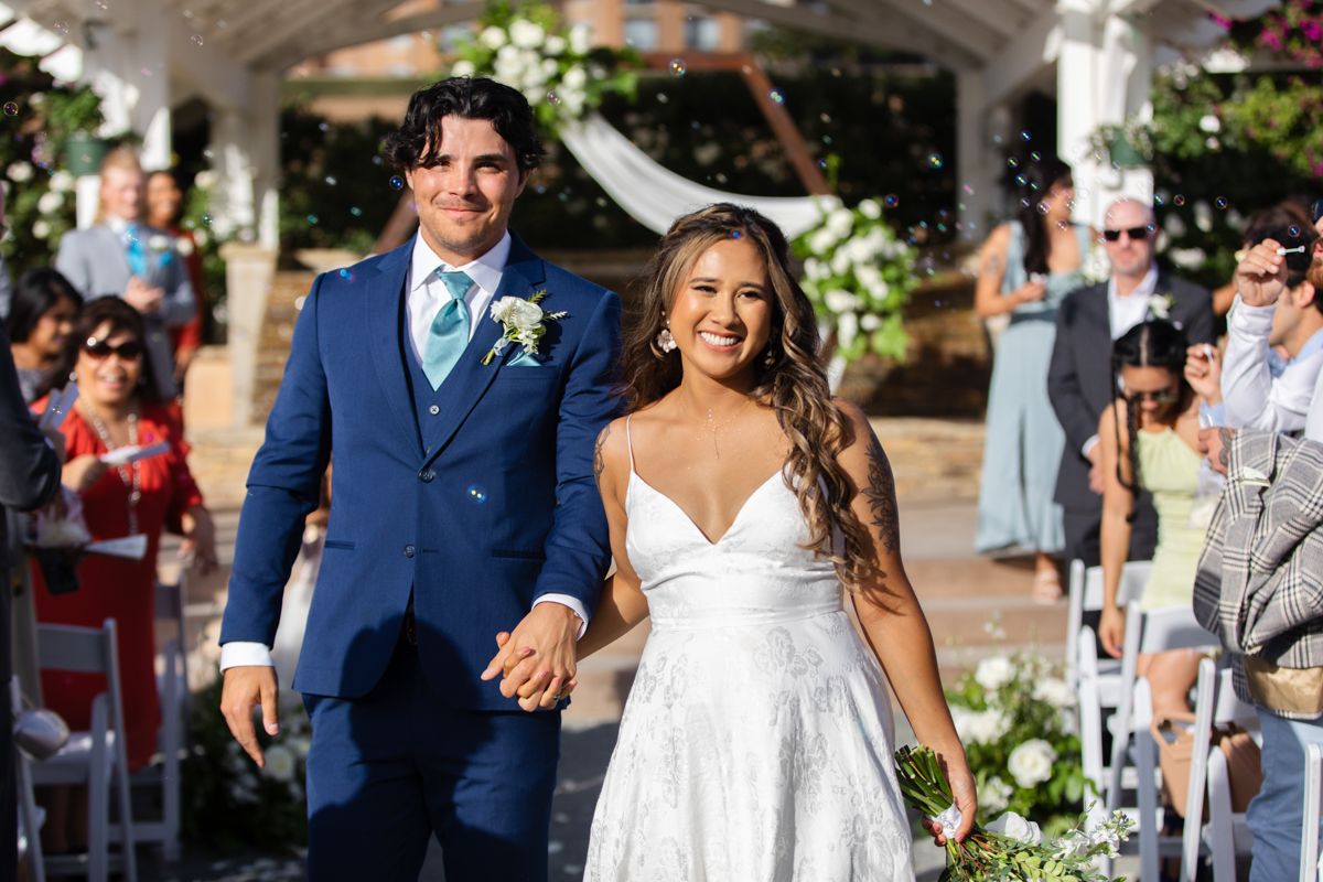 Bride and groom walk down the aisle hand in hand after wedding ceremony outdoors.