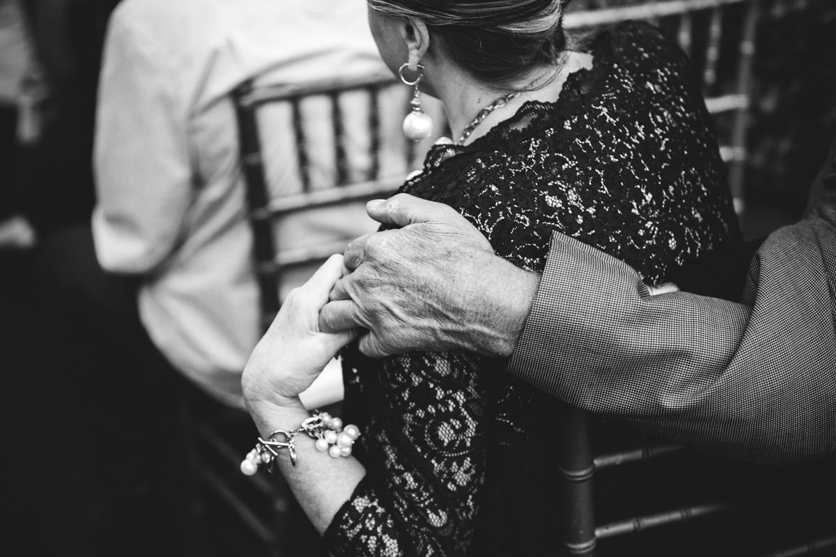 Black and white photo of elderly women holding hands tenderly during wedding ceremony.