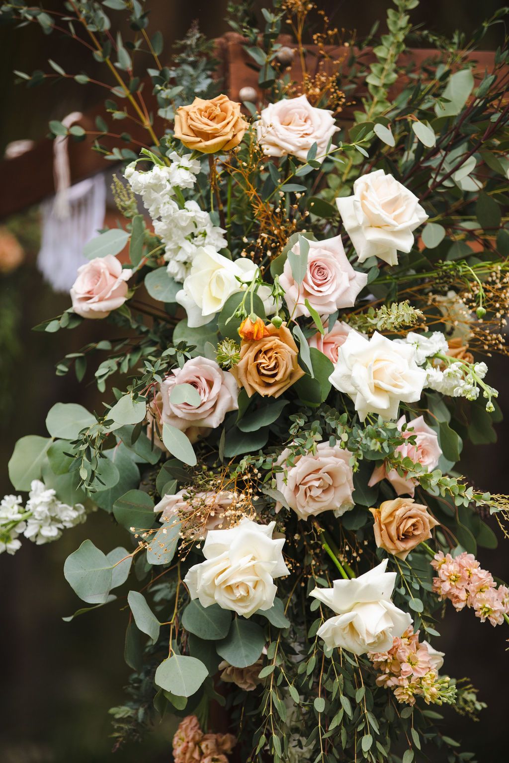 Elegant wedding arch floral arrangement featuring peach, blush, and white roses with eucalyptus greenery.