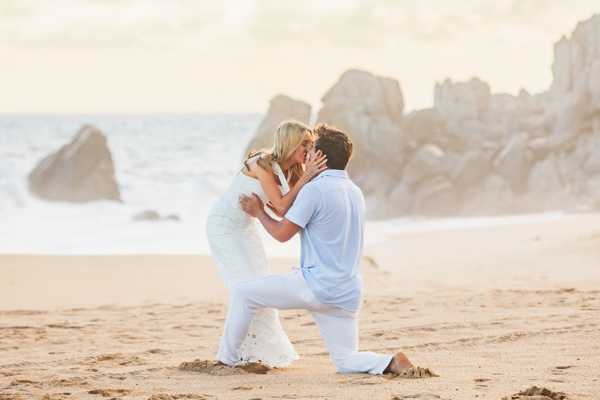 Couple sharing a romantic kiss on the beach after a marriage proposal at golden sunset.