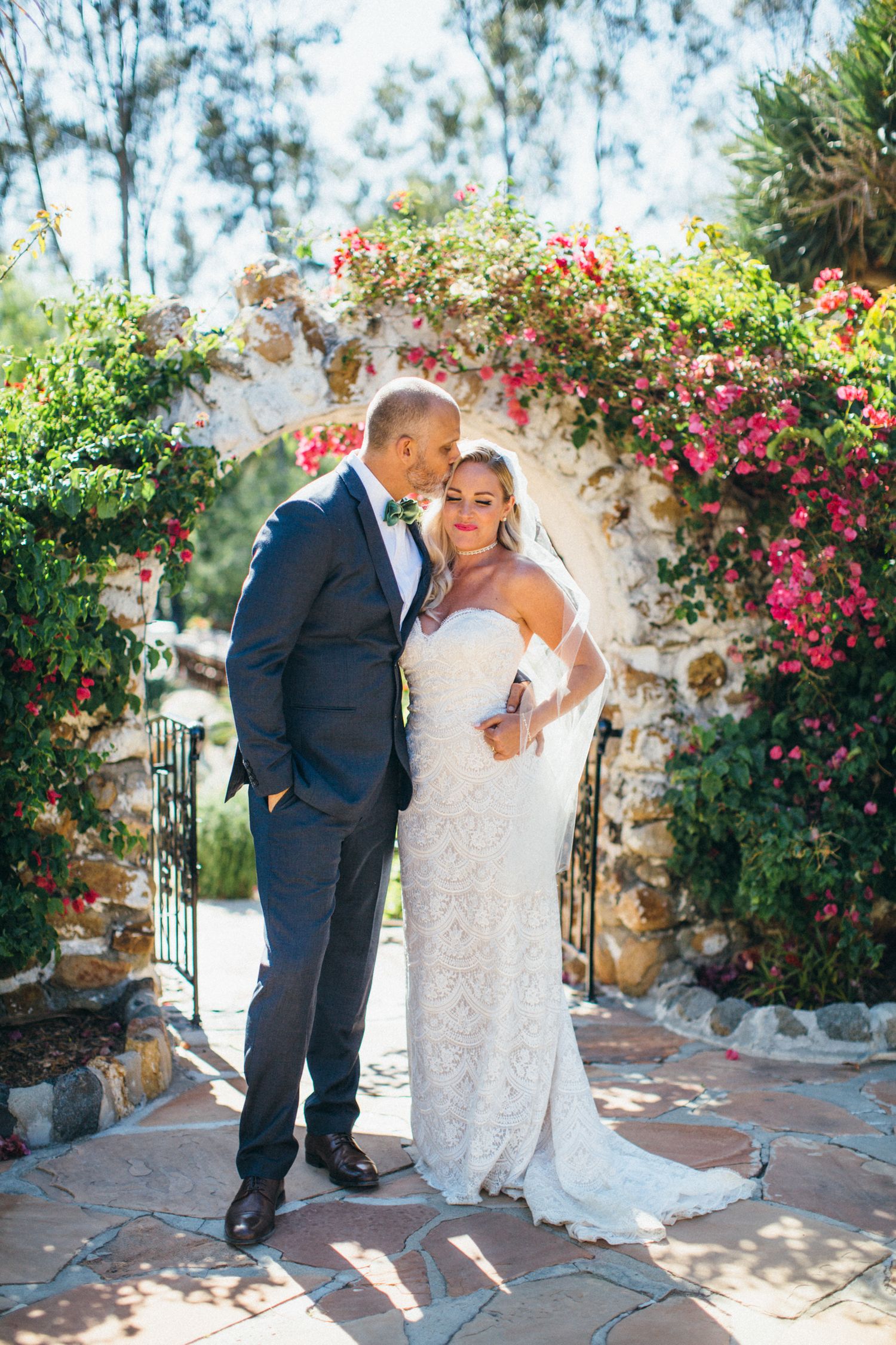 Bride and groom embrace under a floral arch with pink bougainvillea at leo Carrillo ranch