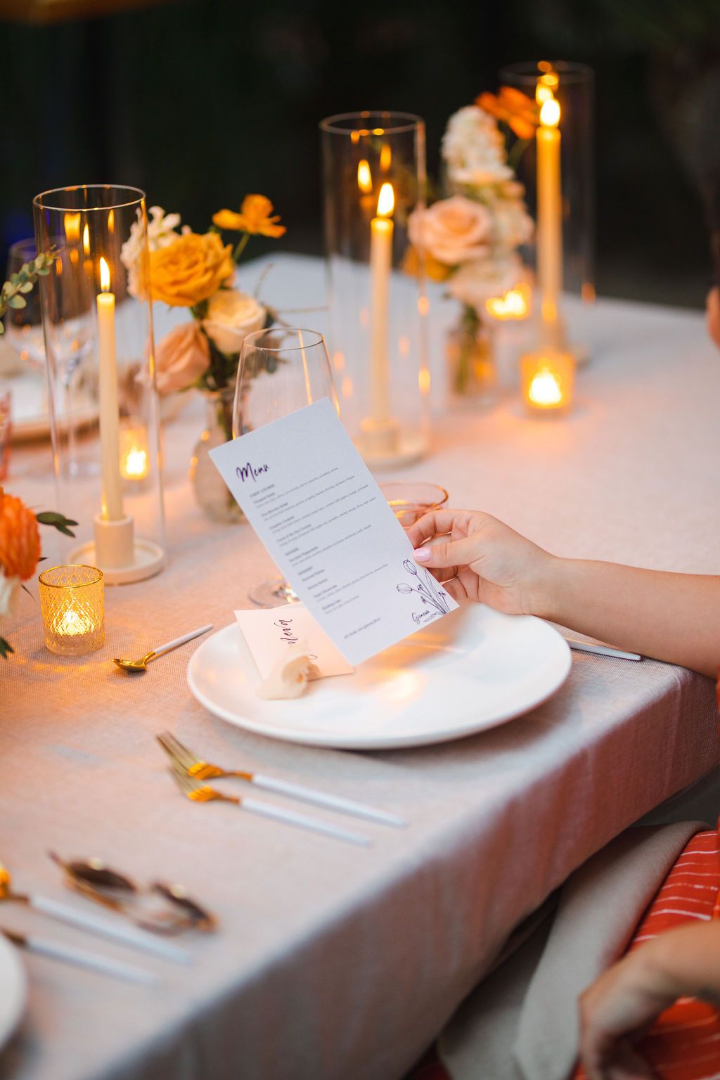 Guest reading a wedding dinner menu card at a candlelit reception table with floral centerpieces.