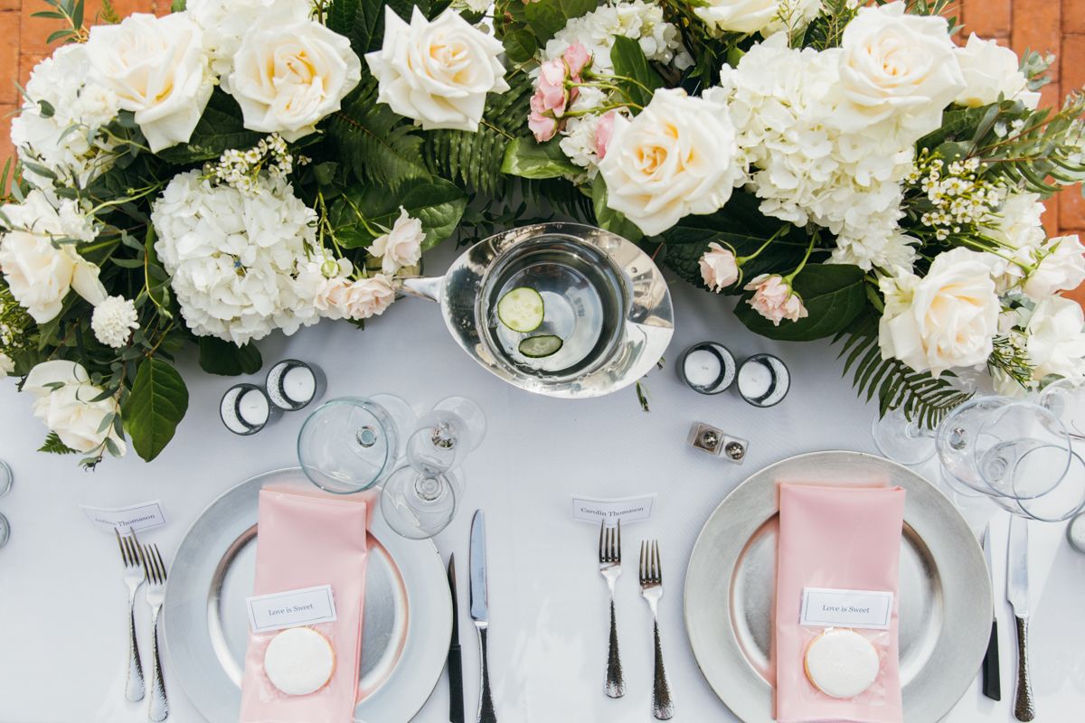 Elegant wedding tablescape with white roses, hydrangeas, pink napkins, and silver accents.