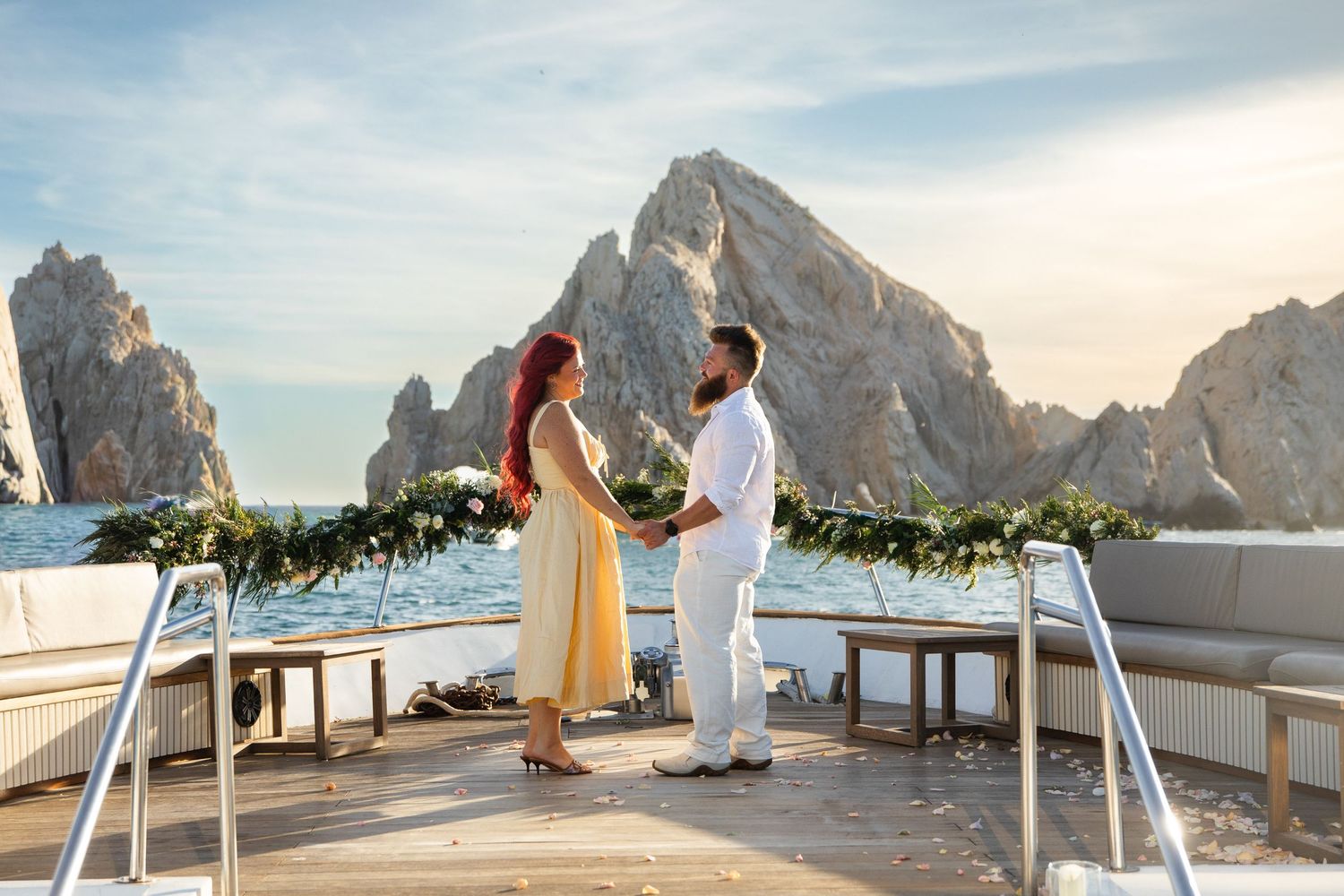 Couple exchanging vows on a luxury yacht deck with iconic Cabo San Lucas rock formations in the background.