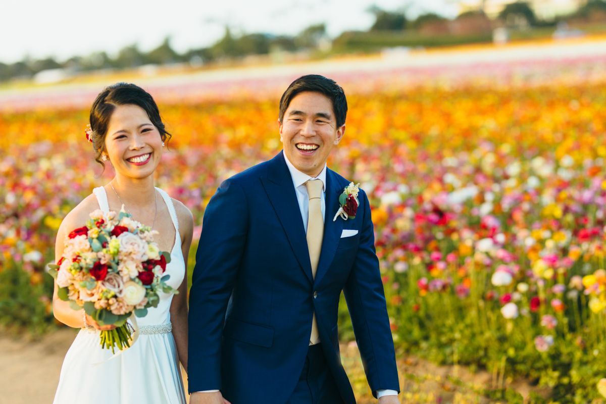 Laughing bride and groom posing together in a colorful ranunculus flower field.