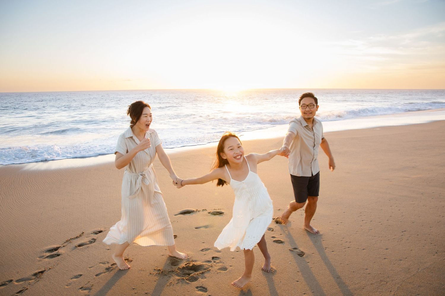 Family of three holding hands and running joyfully on a sandy beach in Cabo San Lucas